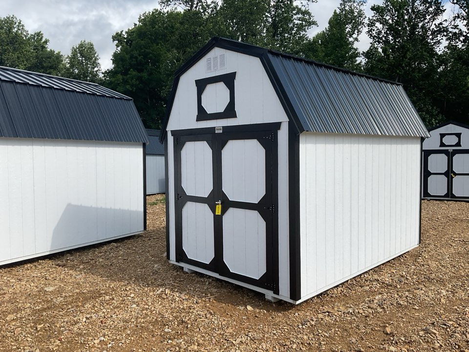 White lofted barns with black trim lined up on the gravel lot
